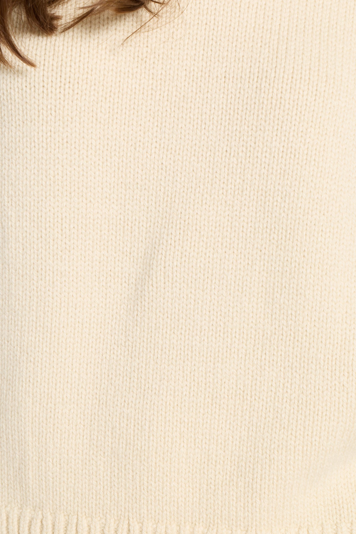 Close-up of a cream-colored knit fabric texture, showing the fine ribbed weave and a small portion of brown hair at the top edge.