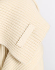 Close-up of a cream-colored ribbed knit garment with a blank rectangular fabric label sewn onto the shoulder.