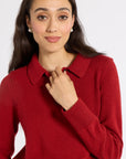 A woman wearing a red knit polo sweater, posing against a light gray studio background.