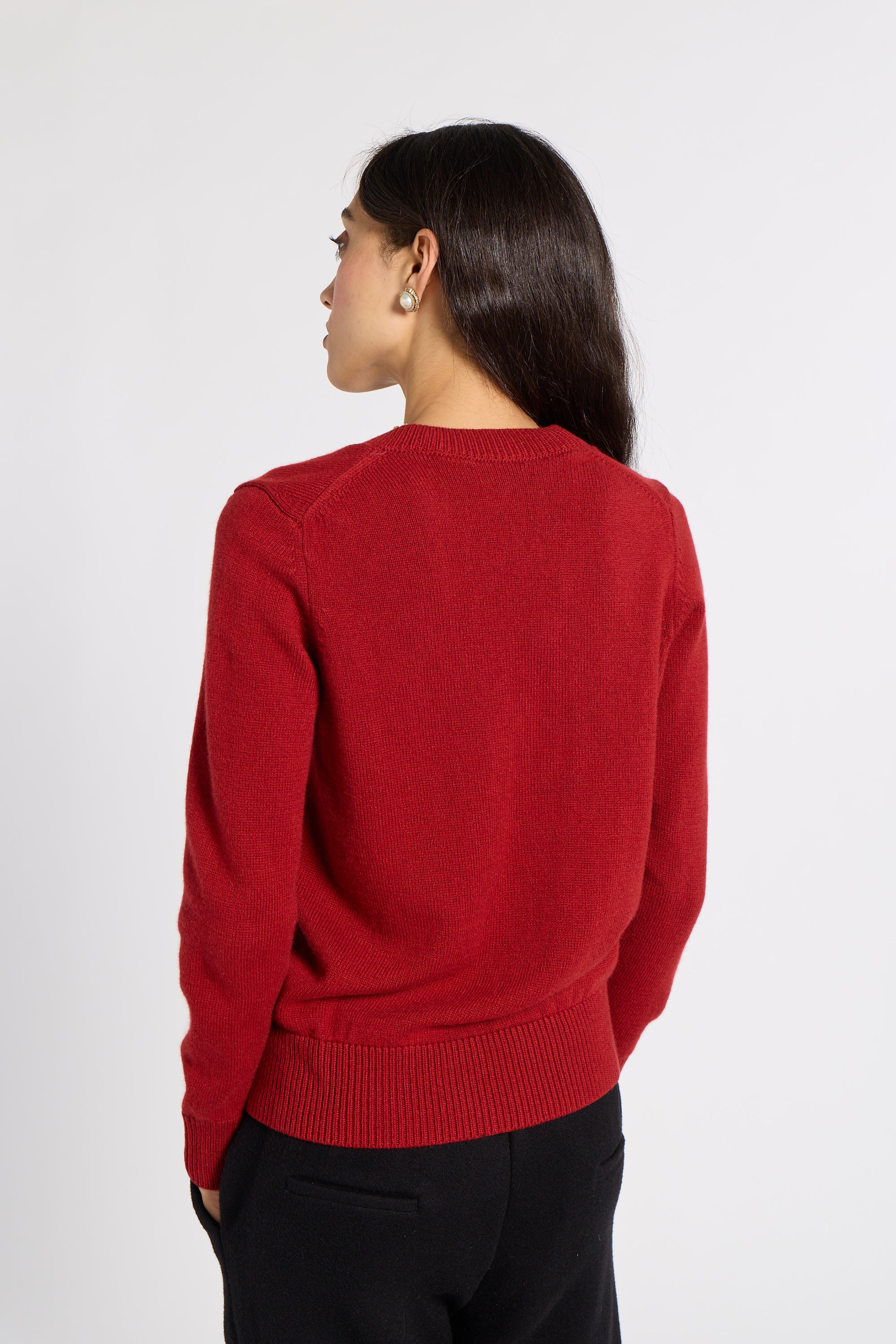 A woman shown from the back wearing a red knit sweater and black trousers, photographed against a plain light gray studio background.