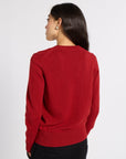 A woman shown from the back wearing a red knit sweater and black trousers, photographed against a plain light gray studio background.