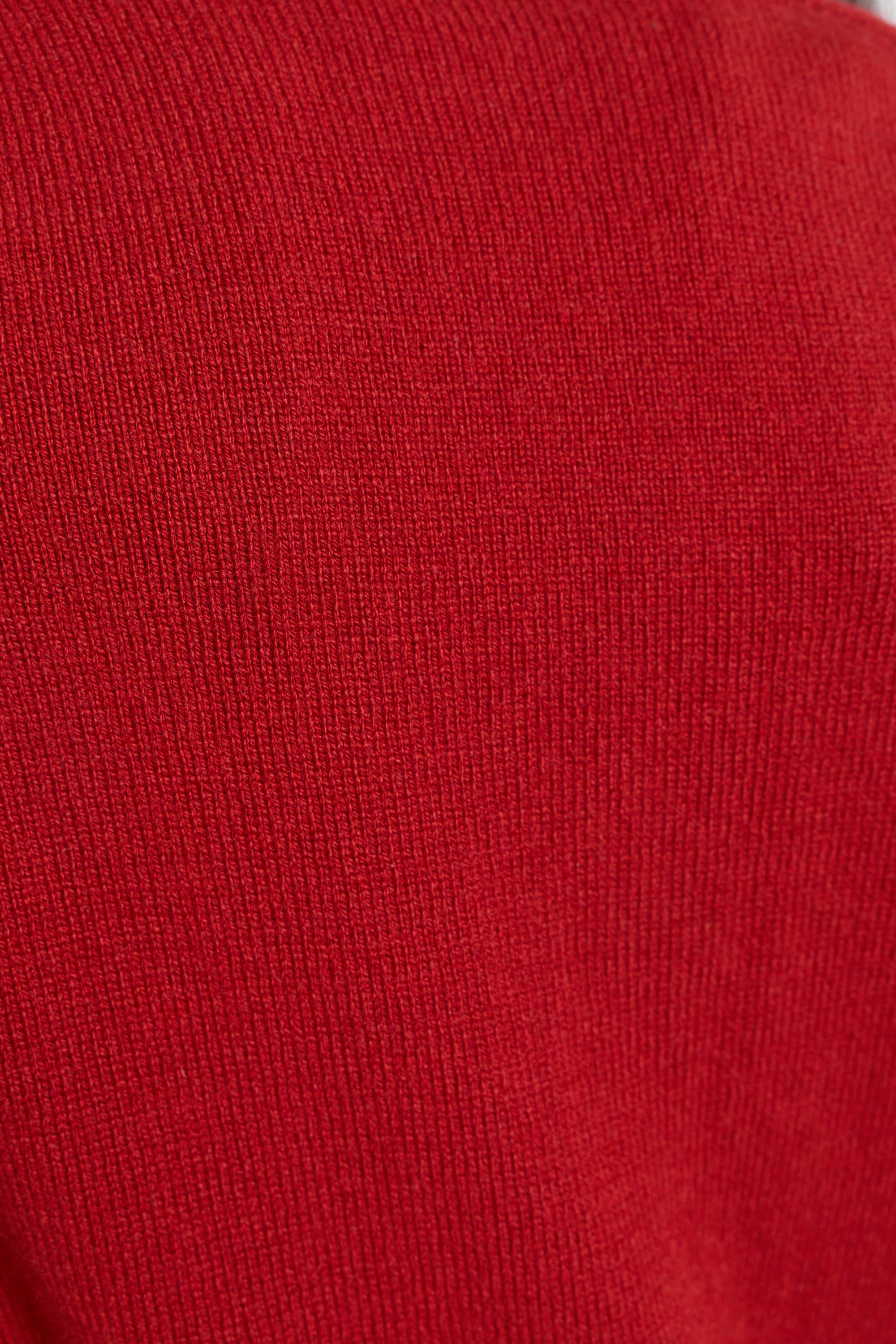 A close-up of a red ribbed knit cashmere texture, showing the detailed weave pattern.