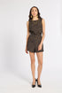 A woman modeling a sleeveless black romper with a textured gold geometric pattern, paired with gold jewelry and black heels, against a plain white studio background.