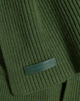 Close-up of a ribbed olive green knit garment with a small dark green leather brand tab reading 'Fleury's Army Co.'