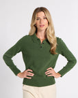 A woman modeling a dark green long-sleeve knit polo sweater with a three-button placket, paired with beige trousers, against a plain light gray studio background.