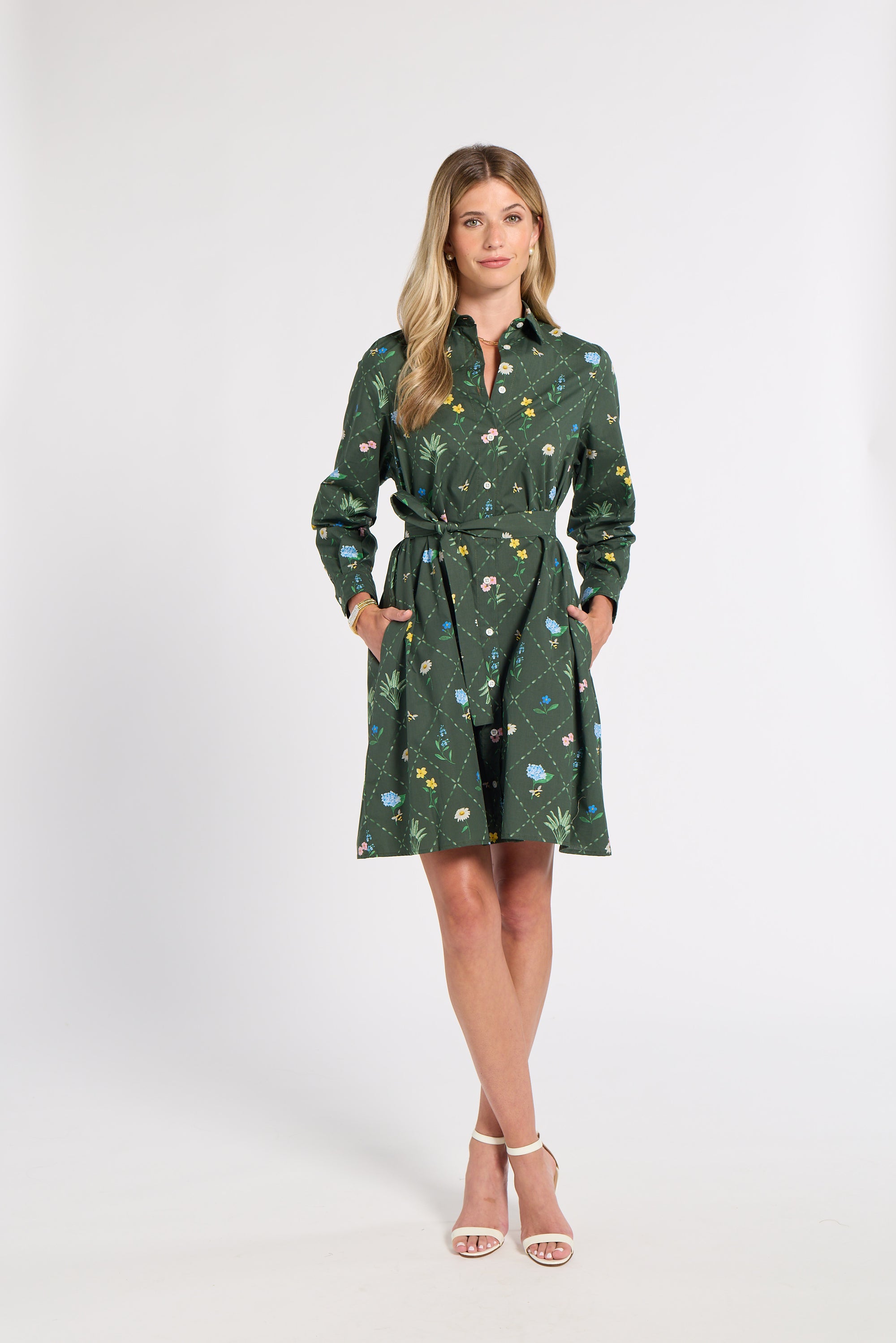 A woman modeling a dark green long-sleeve shirt dress with a colorful floral print, standing against a plain white studio background.