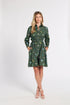 A woman modeling a dark green long-sleeve shirt dress with a colorful floral print, standing against a plain white studio background.