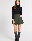 Woman in a studio modeling a black turtleneck with green shorts
