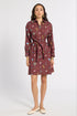 A woman modeling a long-sleeve, collared wrap dress with a tie waist. The dress has a dark reddish-brown base color with a colorful floral and botanical print.