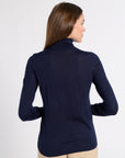 A woman shown from the back wearing a dark navy long-sleeve turtleneck top and beige pants, photographed against a light gray studio background.