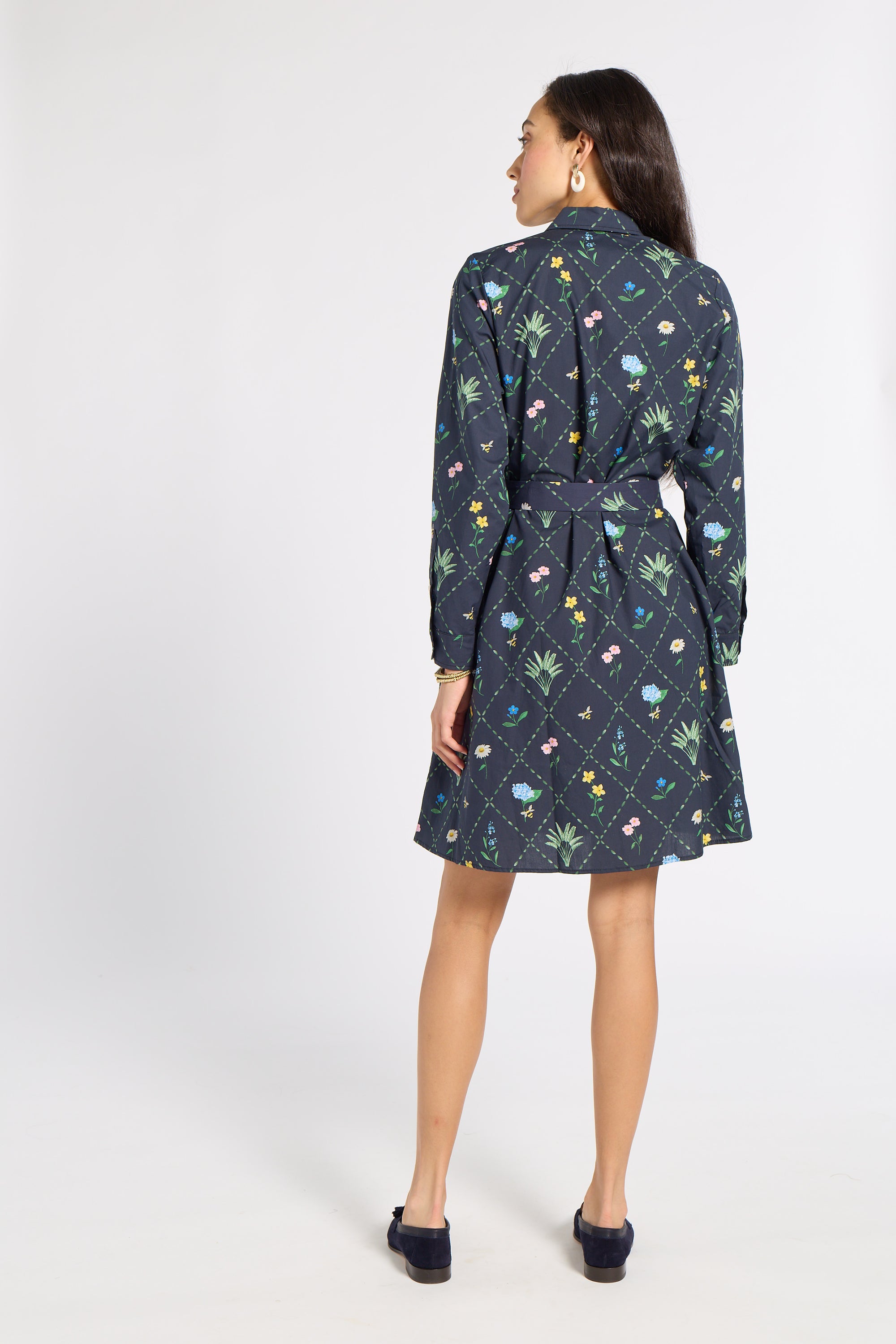A woman is shown from the back wearing a dark navy blue long-sleeve mini dress with a colorful floral and geometric print, featuring a matching tie belt at the waist.