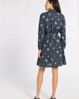 A woman is shown from the back wearing a dark navy blue long-sleeve mini dress with a colorful floral and geometric print, featuring a matching tie belt at the waist.