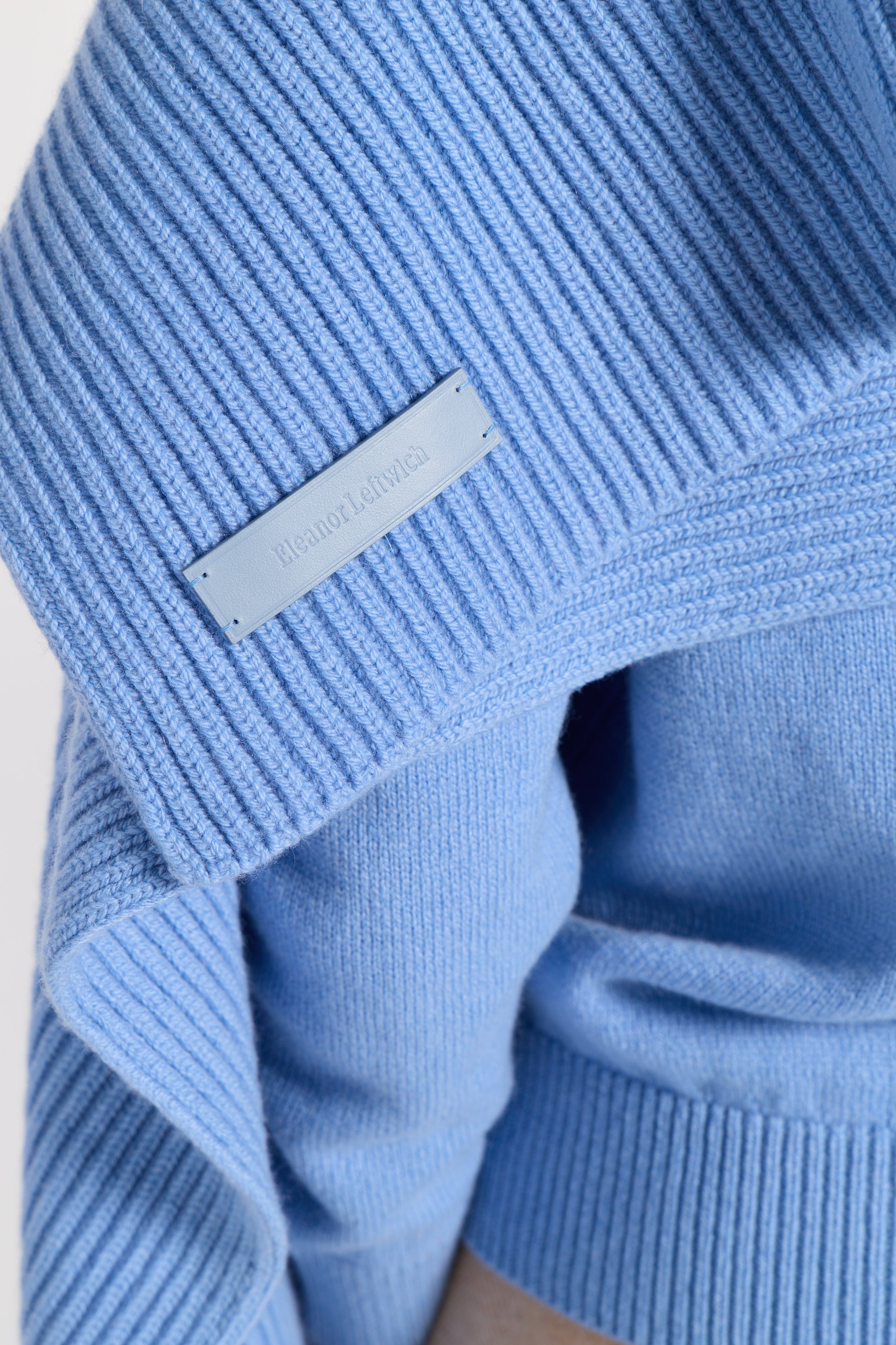 Close up image of a blue cashmere sweater with a leather label that says Eleanor Leftwich