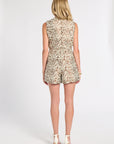 A woman viewed from the back wearing a sleeveless blouse and shorts with an allover abstract floral pattern in beige, brown, and cream, paired with white high-heeled sandals against a light gray studio background.