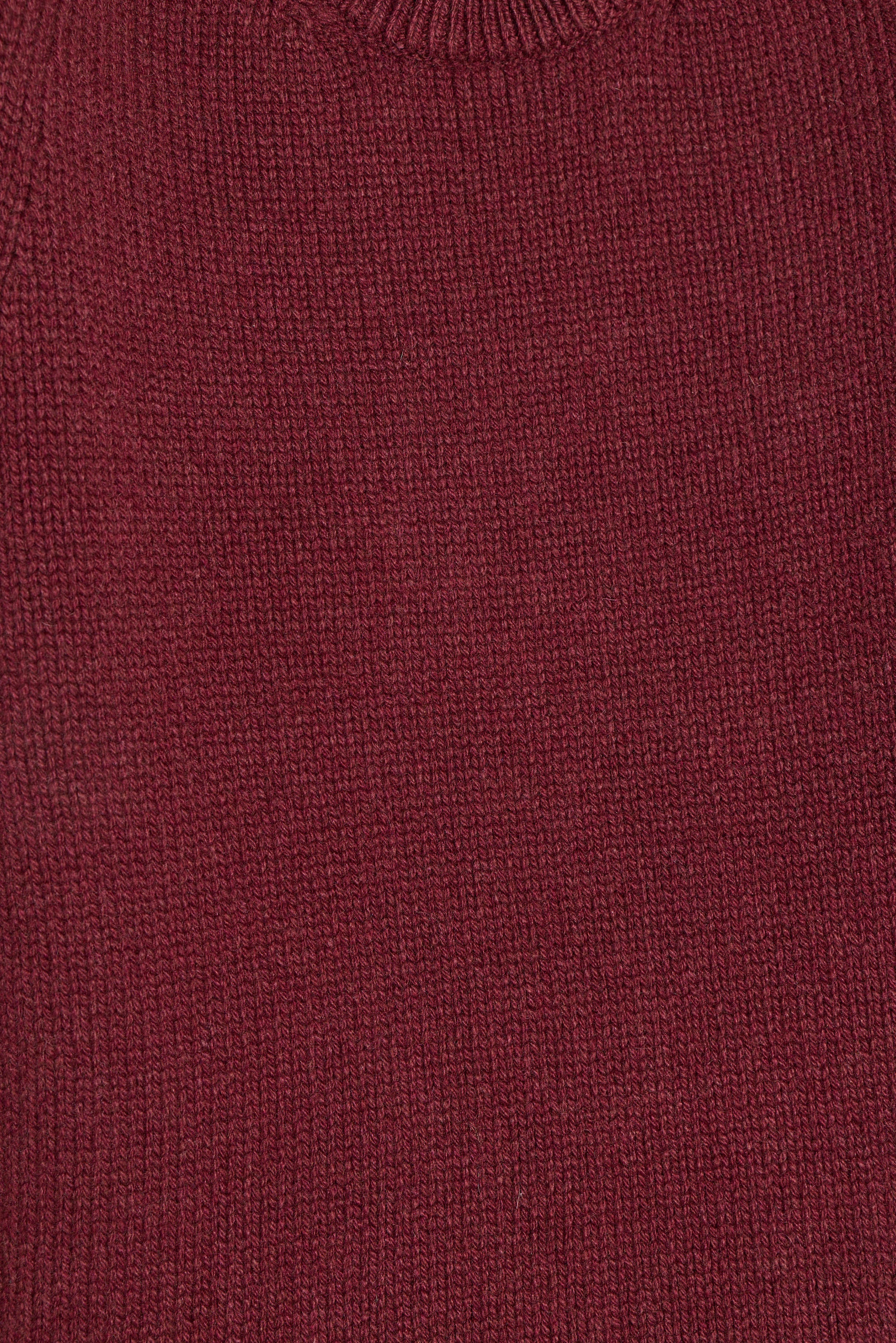 Close-up of a ribbed knit sweater in a deep burgundy red color, showing the detailed texture of the yarn.