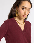 woman modeling a burgundy v neck sweater with gold jewelry on a white backgroun