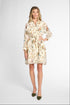 A woman modeling a long-sleeve cream-colored shirt dress with a multicolor floral print and a matching tie belt, paired with olive green pointed-toe flats, against a light gray studio background.