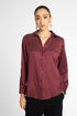 A woman modeling a long-sleeve button-up blouse with vertical stripes in a deep burgundy and maroon shade, paired with black pants, against a light gray studio background.