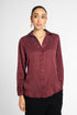 A woman modeling a long-sleeve button-up blouse with vertical pleats in a deep burgundy color, paired with black pants, against a light gray studio background.