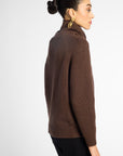 Side view: woman wearing a turtleneck sweater in Chocolate brown with black pants in front of a white background 