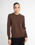 Front view: woman wearing a classic crewneck sweater in Chocolate brown with black pants in front of a white background 