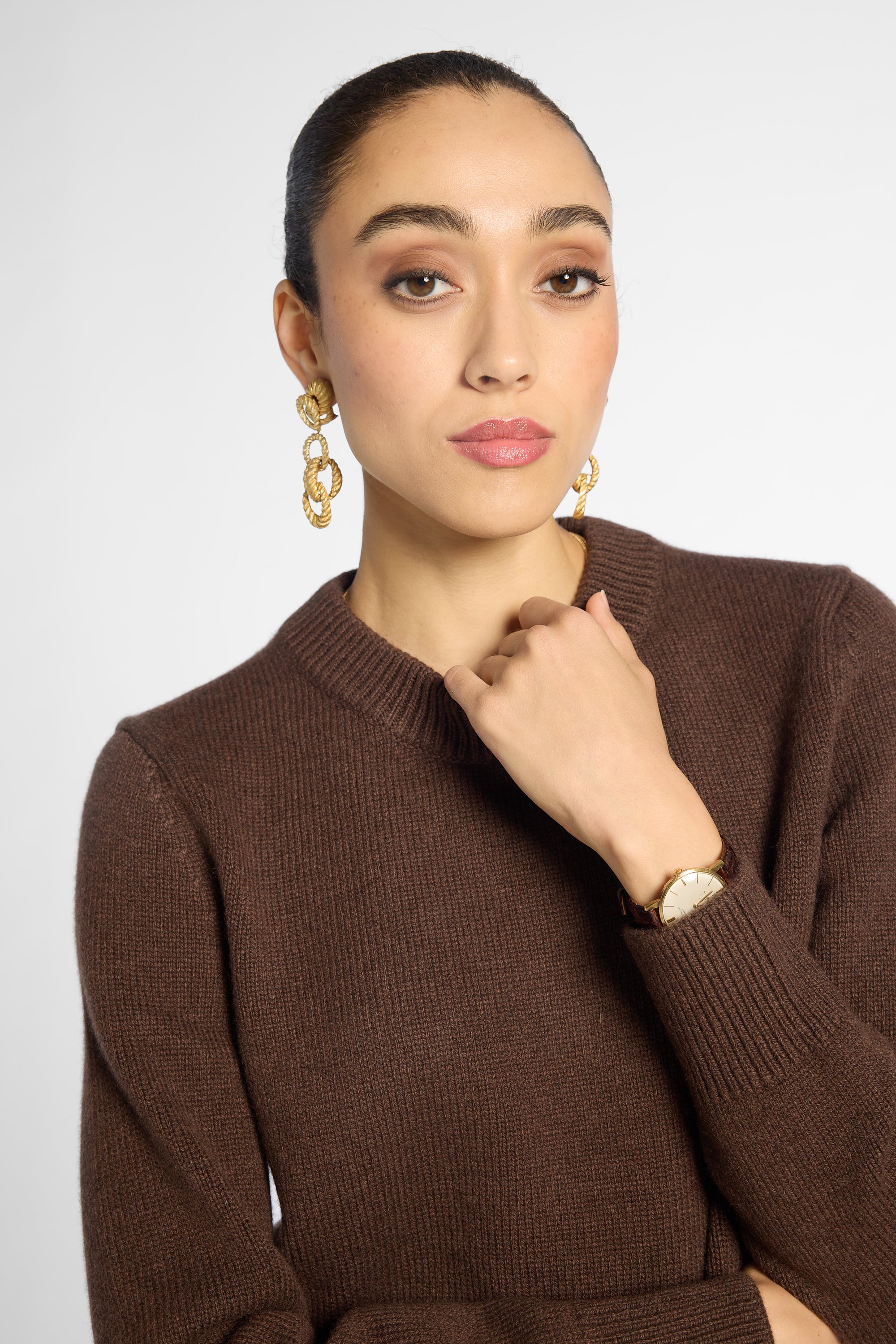 Close view: woman wearing a classic crewneck sweater in Chocolate brown with black pants in front of a white background 