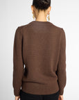 Back view: woman wearing a classic crewneck sweater in Chocolate brown with black pants in front of a white background 
