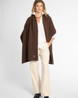 Front View: Woman wearing a chocolate brown wrap on top of a white button up shirt and khakis in front of a white background.
