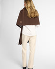 Back View: Woman wearing a chocolate brown wrap on top of a white button up shirt and khakis in front of a white background.
