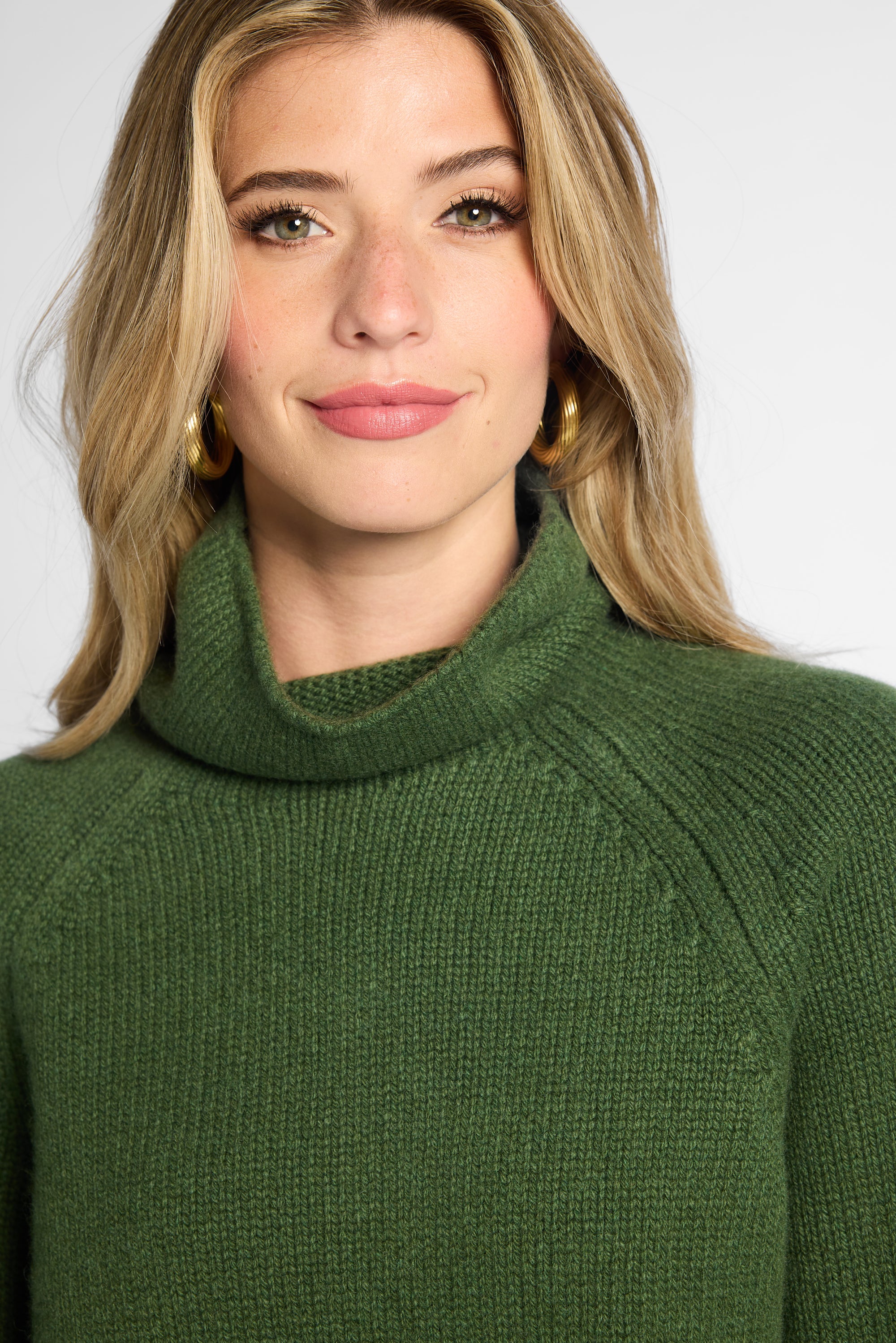Close view: Woman wearing Forest Green boyfriend turtleneck sweater in front of white background. 
