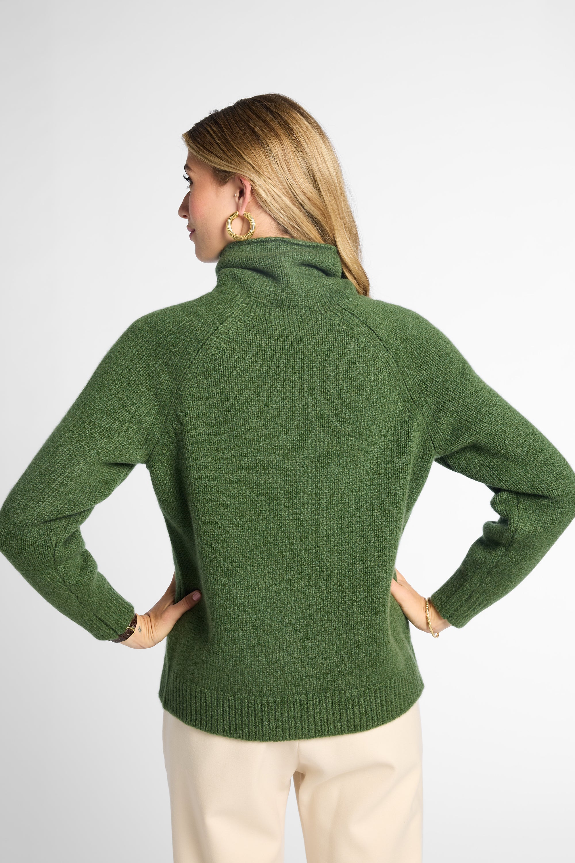 Back view: Woman wearing Forest Green boyfriend turtleneck sweater in front of white background. 