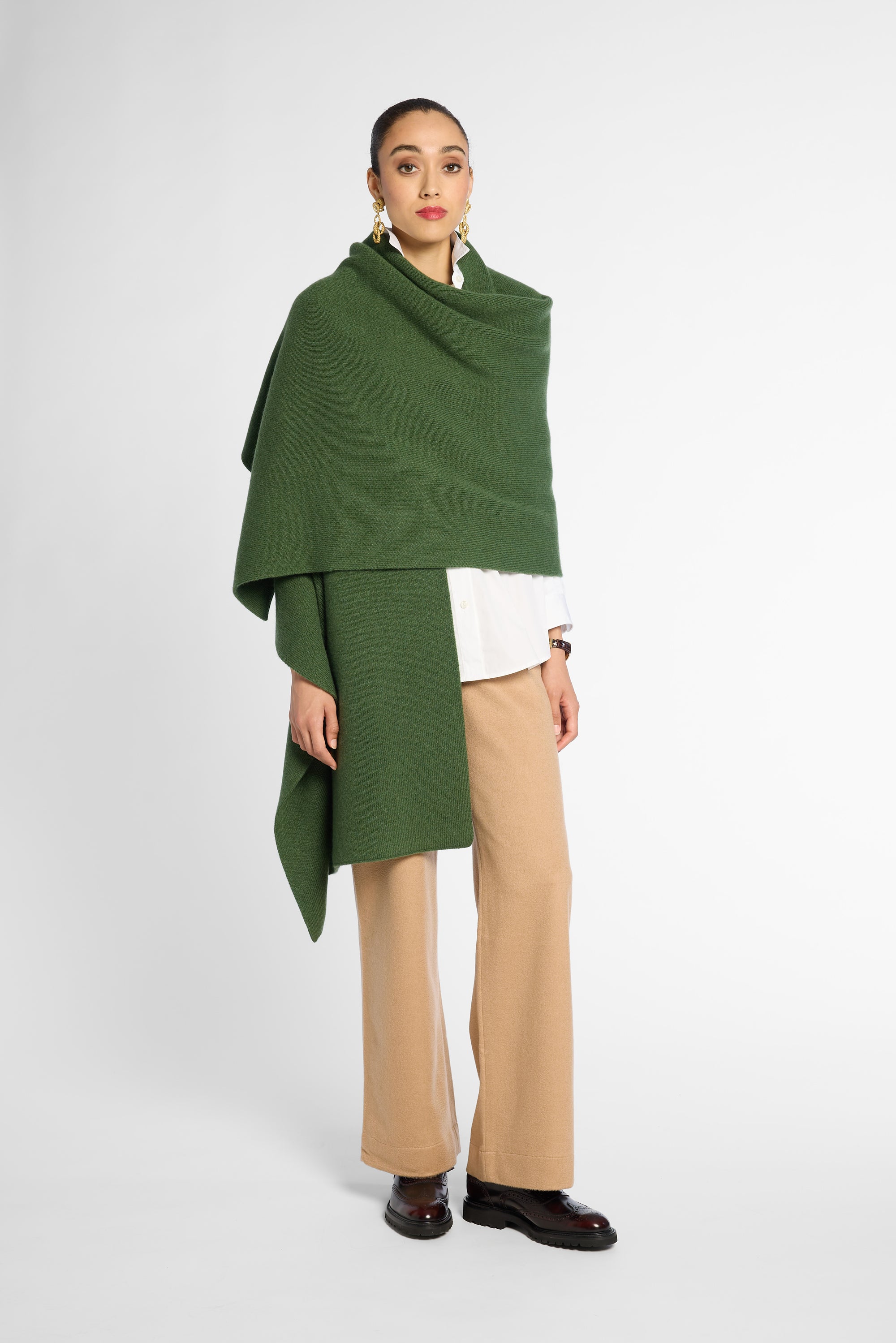 Another view of women wearing a Forest Green cashmere wrap over a white shirt and tan pants in front of a white background. Embossed green leather patch shown on the corner.