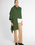 Another view of women wearing a Forest Green cashmere wrap over a white shirt and tan pants in front of a white background. Embossed green leather patch shown on the corner.