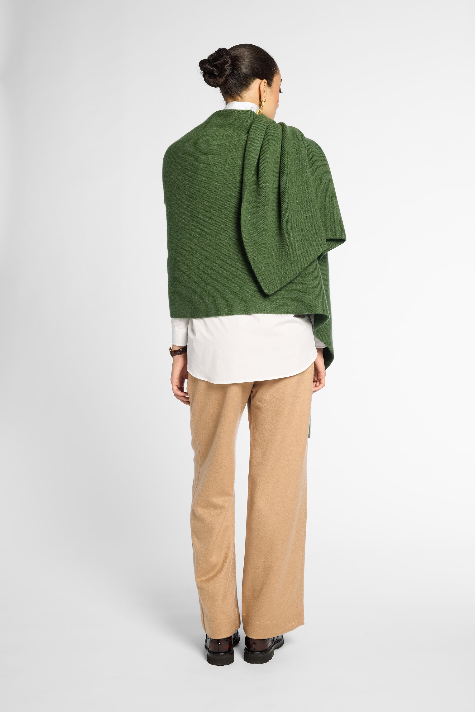 Back view of women wearing a Forest Green cashmere wrap over a white shirt and tan pants in front of a white background. Embossed green leather patch shown on the corner.