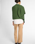 Back view of women wearing a Forest Green cashmere wrap over a white shirt and tan pants in front of a white background. Embossed green leather patch shown on the corner.
