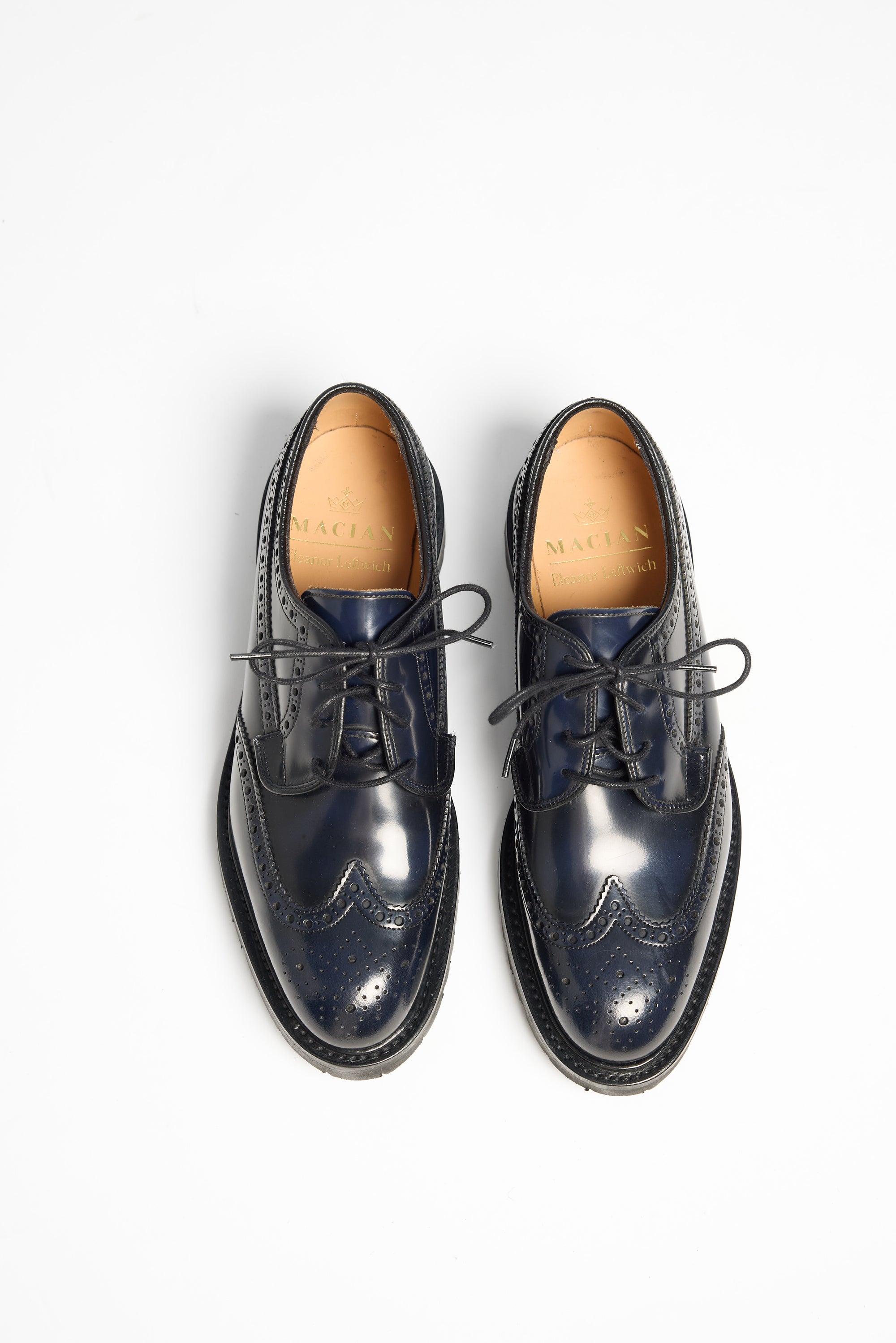 A pair of dark navy blue brogue oxford shoes with black laces, shown from a top-down view on a clean white background. The brand name 'MACKENZIE' is visible on the tan insole of each shoe.