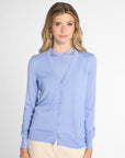 A woman modeling a light blue cardigan sweater and button front, paired with beige pants, against a plain light gray studio background.