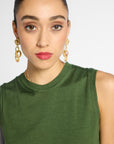 A close-up of a model wearing a sleeveless olive green top and gold chain-link drop earrings against a light gray background.