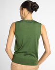 A woman shown from the back wearing a sleeveless green knit top and beige pants against a light gray studio background.