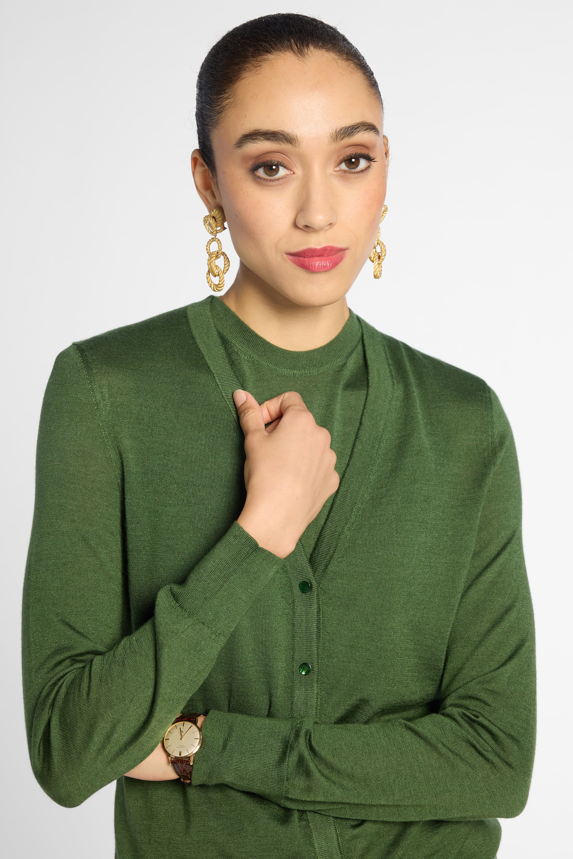 A woman wearing a green long-sleeve knit cardigan with a split neckline and button front, posed against a light gray studio background.