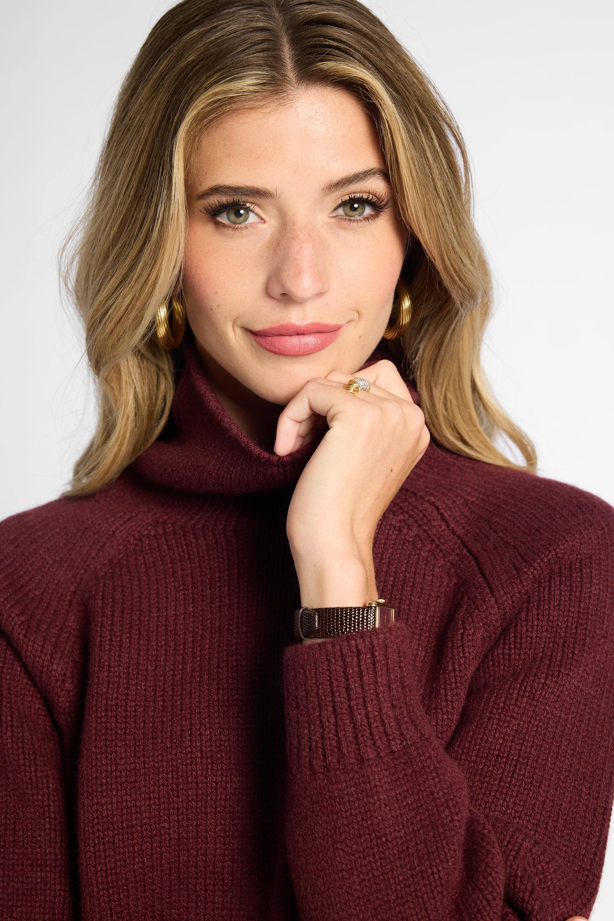 Close up view of woman in wine-colored boyfriend turtleneck sweater in front of a white background.