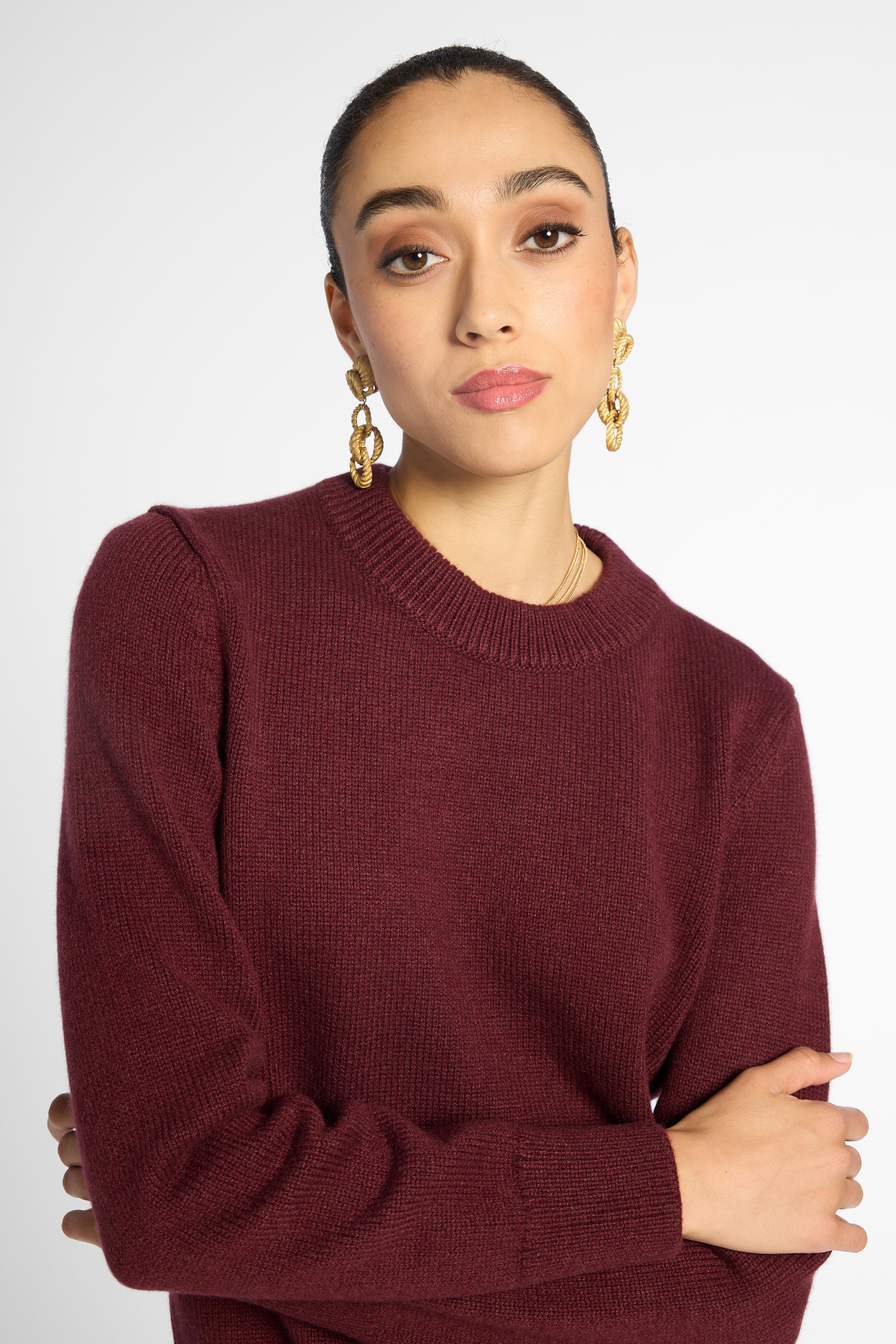 Close up view of woman in wine-colored crew neck cardigan in front of a white background.