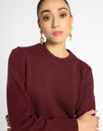 Close up view of woman in wine-colored crew neck cardigan in front of a white background.