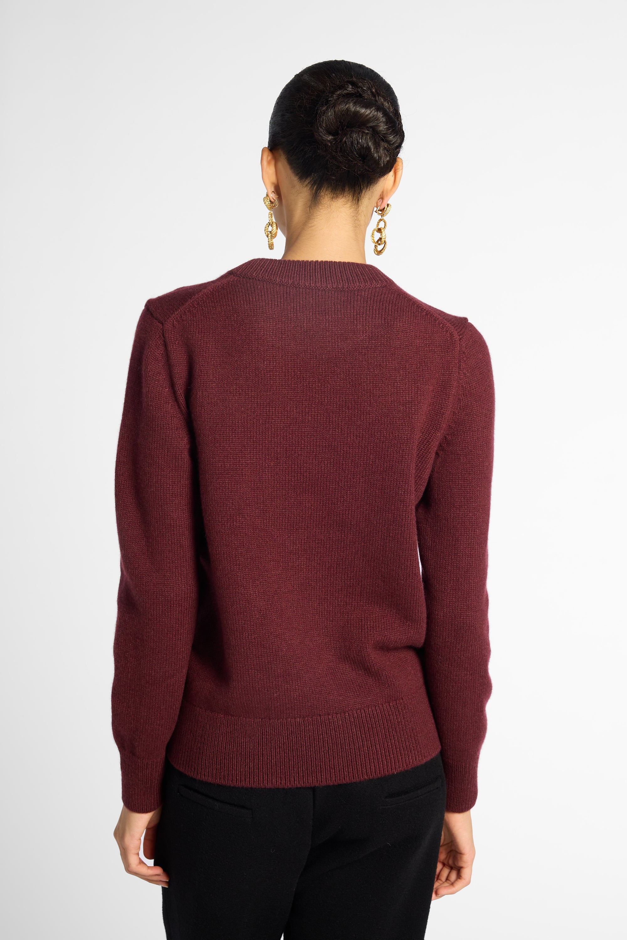 Back view of woman in wine-colored crew neck cardigan in front of a white background.