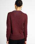 Back view of woman in wine-colored crew neck cardigan in front of a white background.