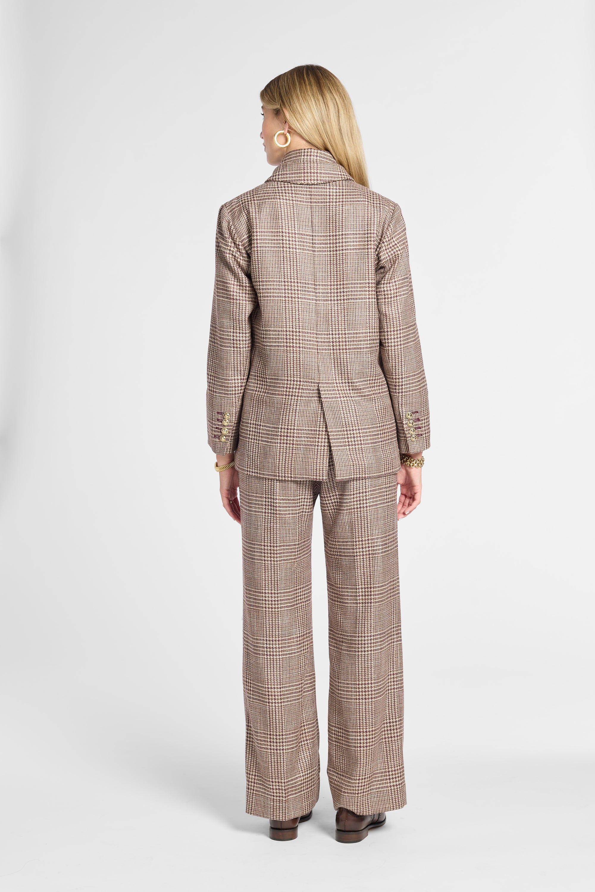 A woman shown from the back wearing a matching brown and beige plaid blazer and wide-leg trousers set, photographed against a clean light gray studio background.