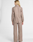 A woman shown from the back wearing a matching brown and beige plaid blazer and wide-leg trousers set, photographed against a clean light gray studio background.