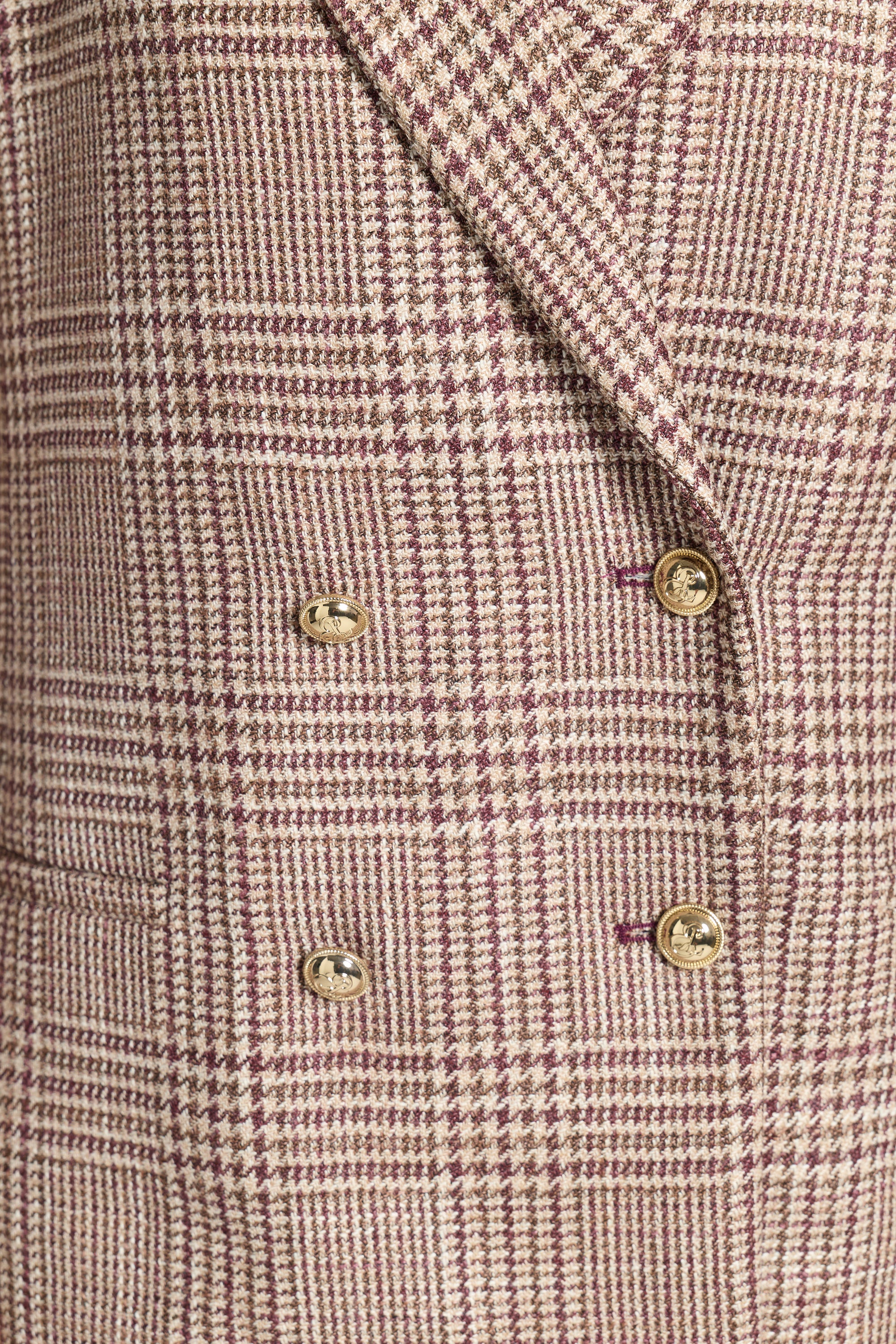 Close-up of a double-breasted blazer in a beige and dusty rose plaid pattern, featuring gold buttons.