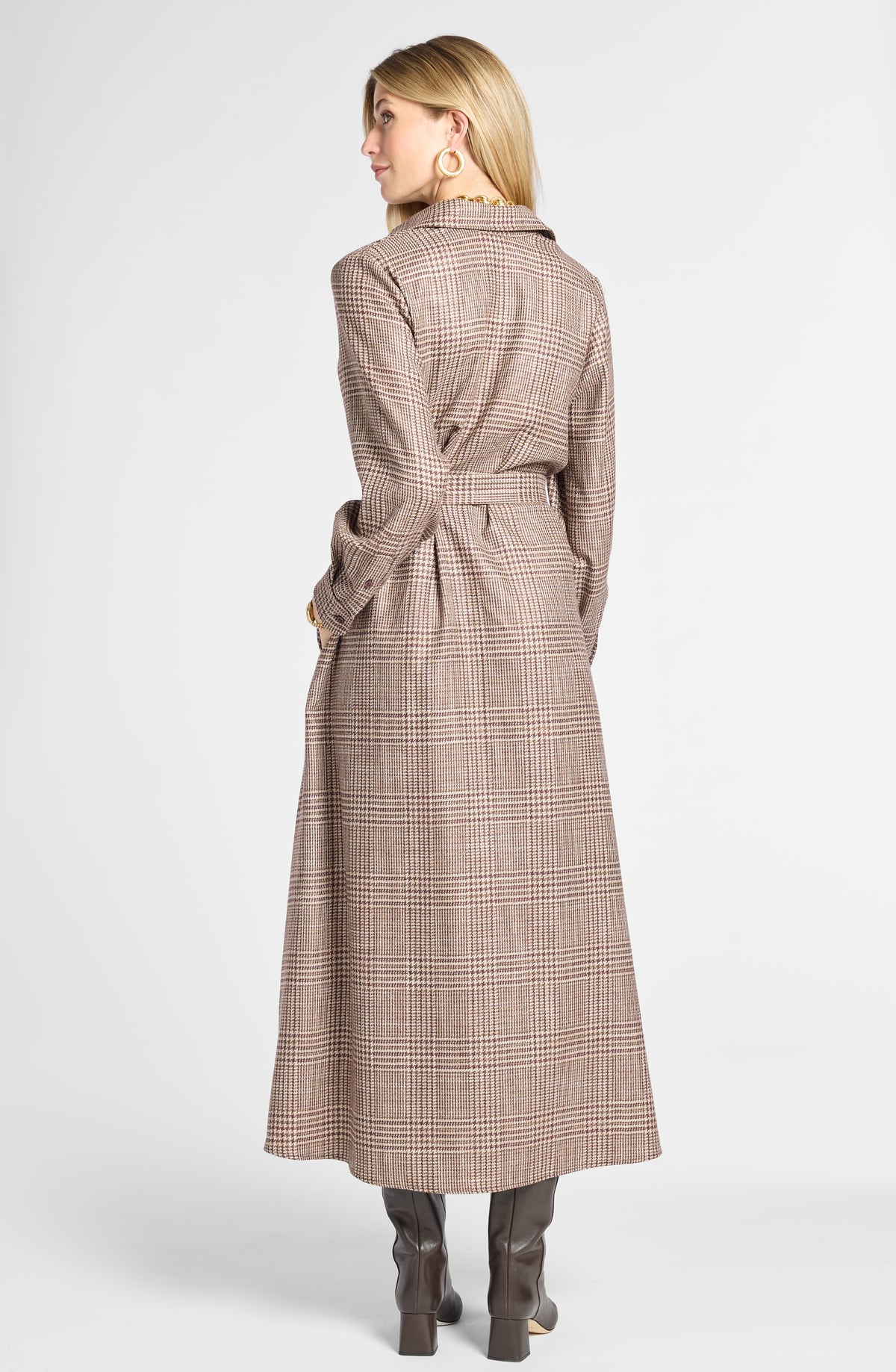 A woman shown from the back wearing a long brown and beige plaid coat with a matching waist tie, paired with dark brown boots, against a light gray studio background.
