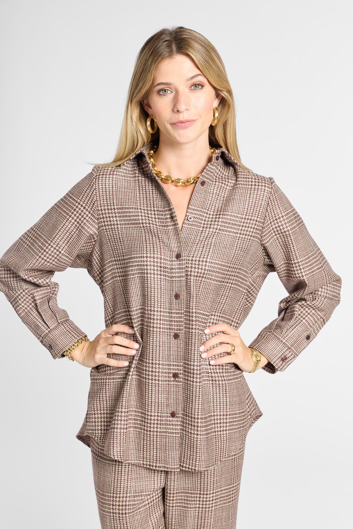 A woman modeling a brown and beige plaid button-up shirt and matching pants set against a light gray studio background.